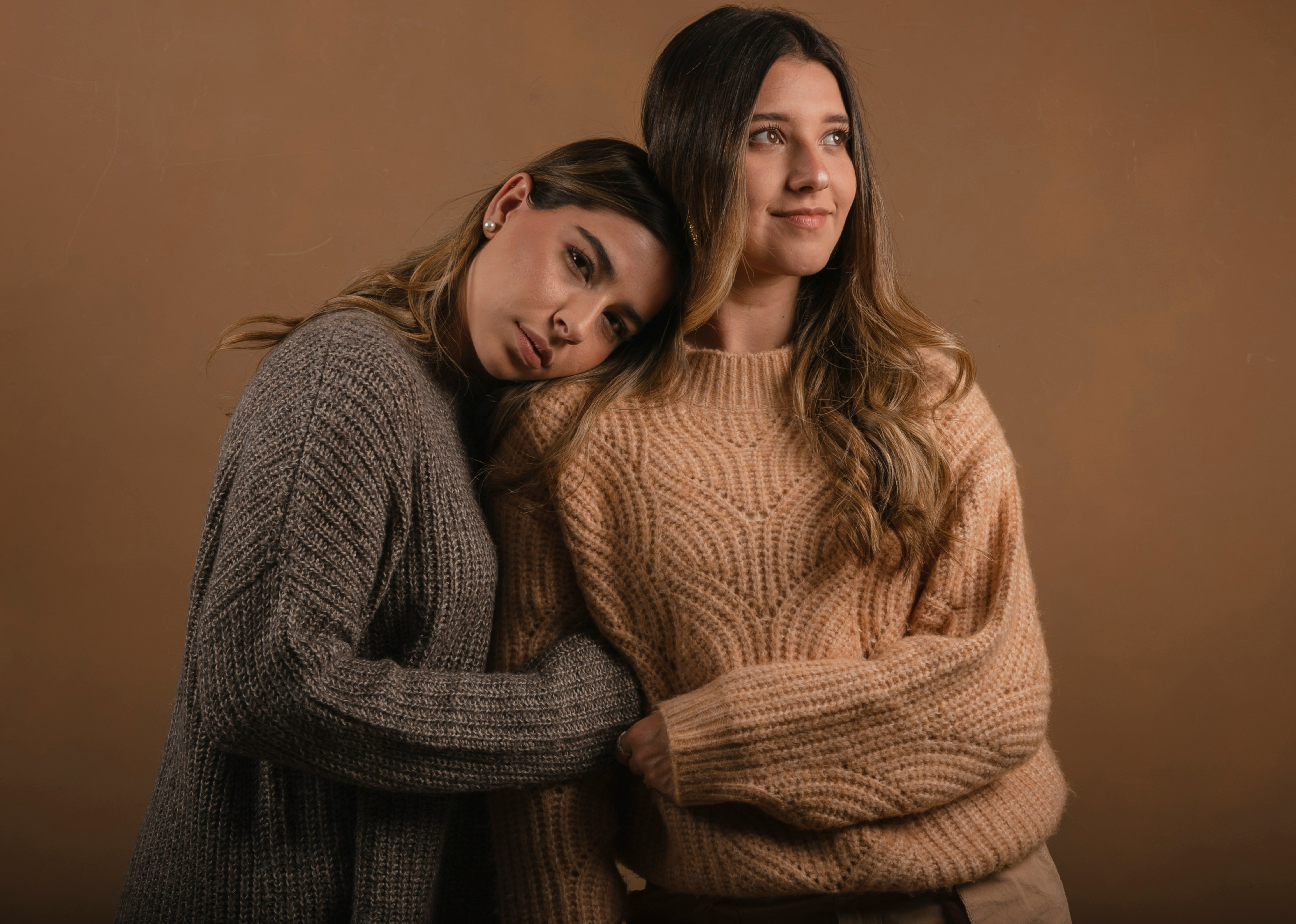 Two women wearing cozy sweaters against a warm brown background